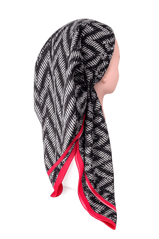 A black and white patterned pretied tichel with a vibrant pink border, styled on a mannequin head against a plain white background.
