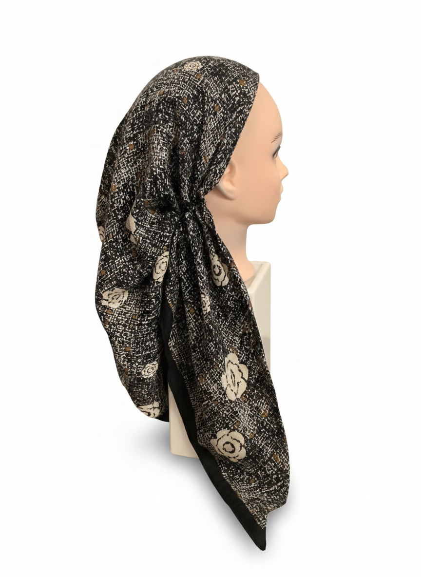 Mannequin head wearing a black headscarf with gold floral patterns on a white background