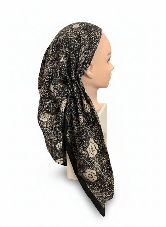 Mannequin head wearing a black headscarf with gold floral patterns on a white background