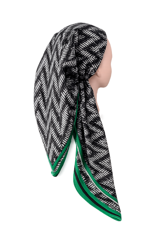 A black and white patterned headscarf with a green border, styled on a mannequin head against a plain white background.