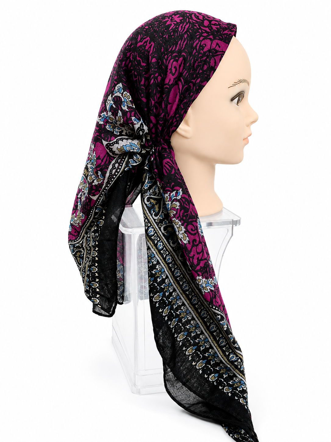A patterned headscarf displayed on a mannequin head and clear stand against a white studio background. The scarf has a black base with a vivid magenta floral pattern and ornate multicolor border detailing.