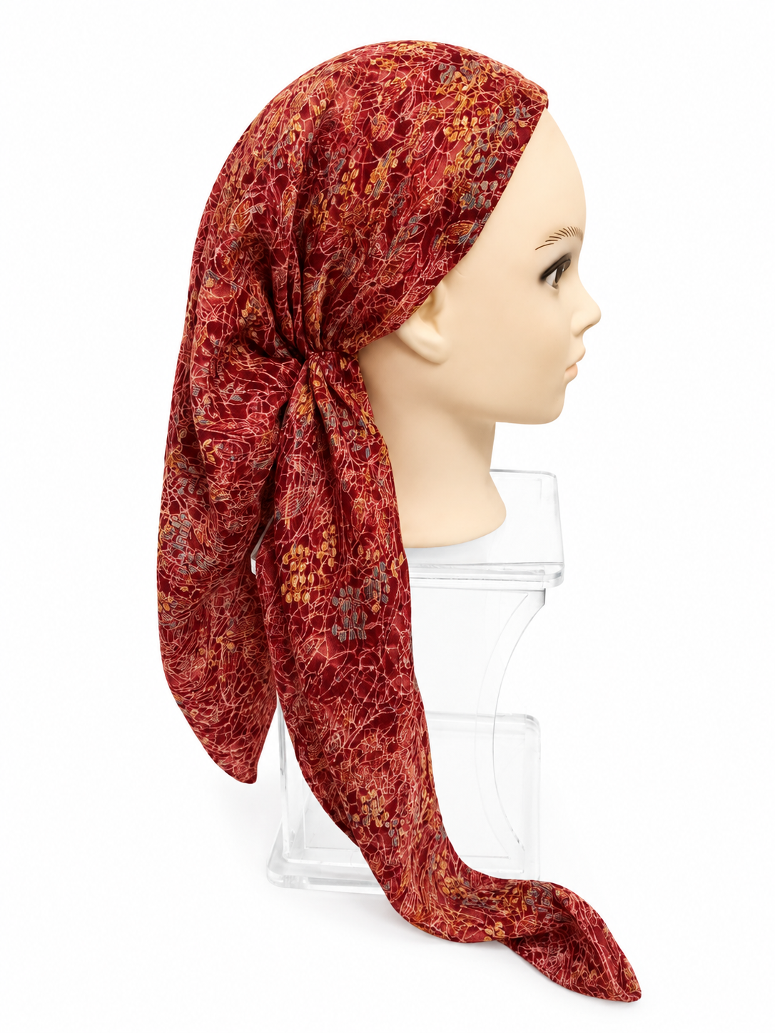 A red patterned headscarf with a floral and abstract print, styled on a mannequin head and displayed on a clear acrylic stand against a white background.