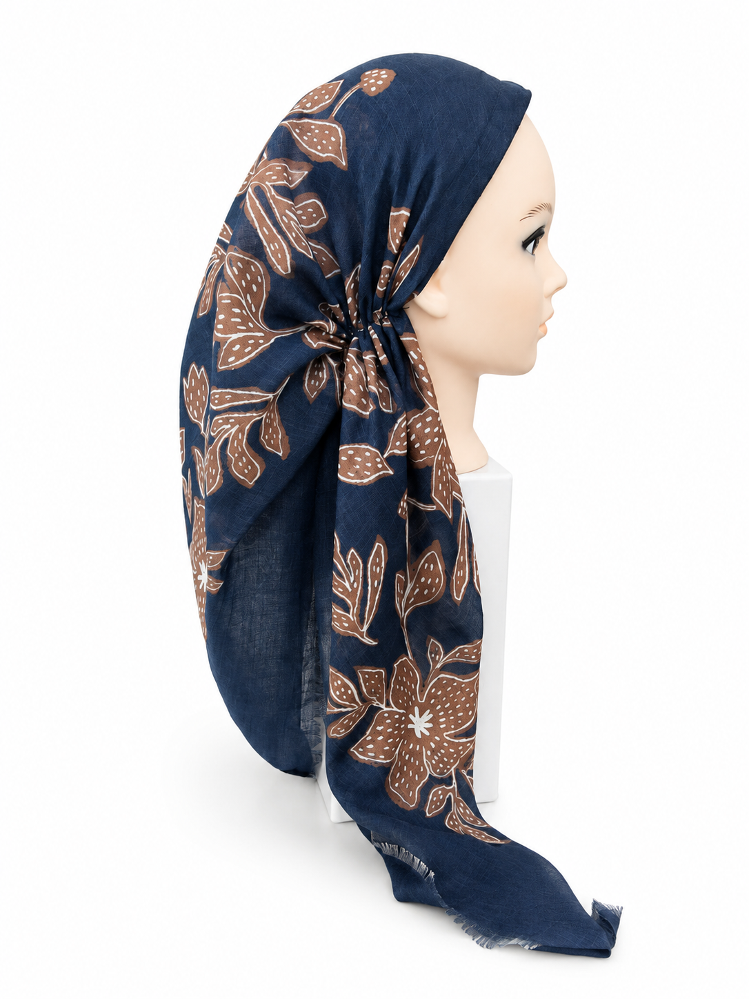 A navy blue headscarf with a brown and beige floral batik pattern, styled on a mannequin head against a white background.