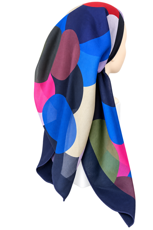 A multicolor hijab scarf with a bold abstract geometric pattern of large overlapping circles in navy, blue, pink, burgundy, beige, and olive green, styled on a mannequin head against a white background.