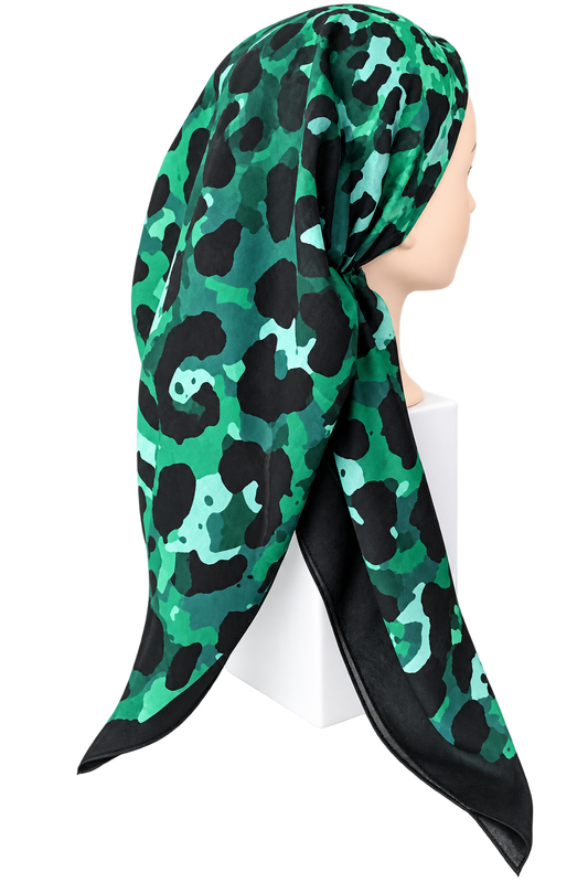 A green and black camouflage-patterned silk scarf styled on a mannequin head, shown against a plain white background.