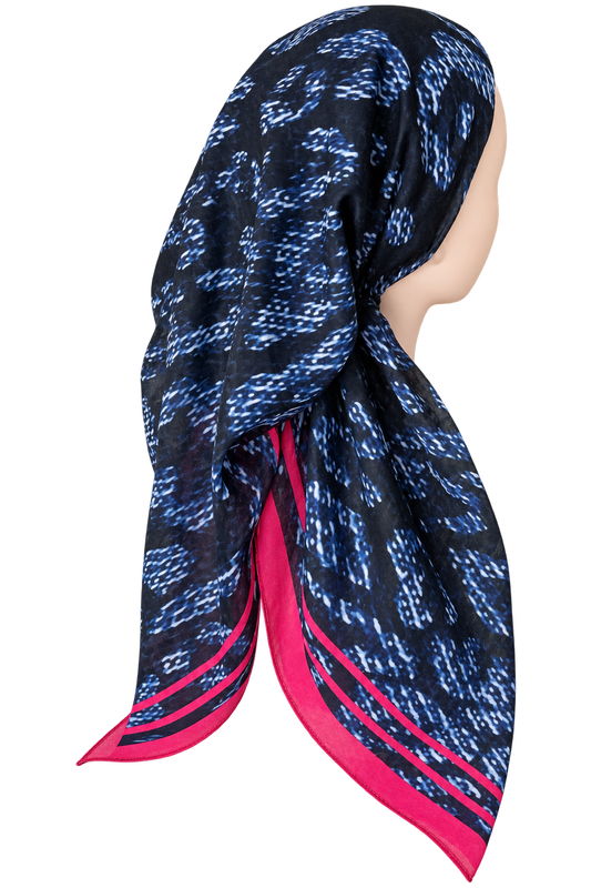 A patterned square scarf displayed on a mannequin head, featuring a black base with blue abstract ikat-like motifs and bright pink border stripes.