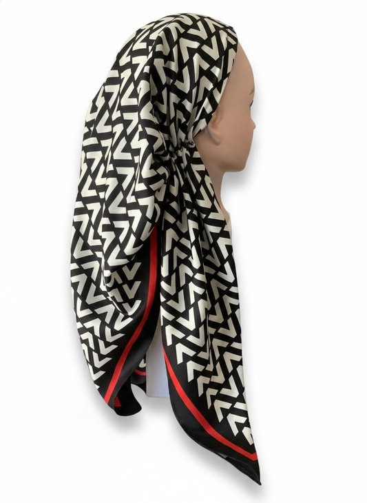 Person wearing a black and white patterned pretied tichel with red accents on a white background